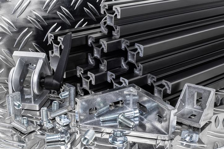 stack of black anodized aluminum extrusion bars, connector, joint, screw , slot nut and angle bracket on silver shiny diamond plate background.